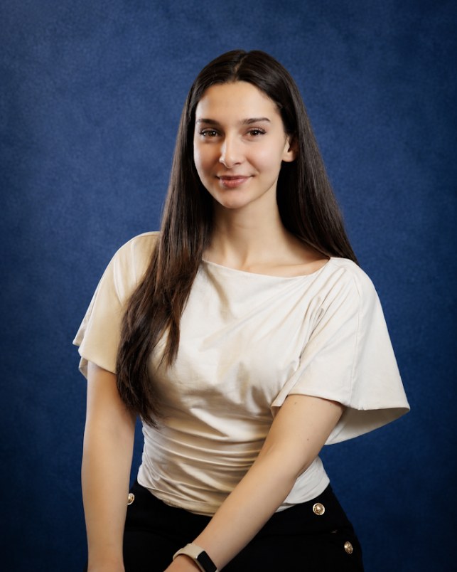Dea Sokoli smiling, in a cream top against a blue backdrop