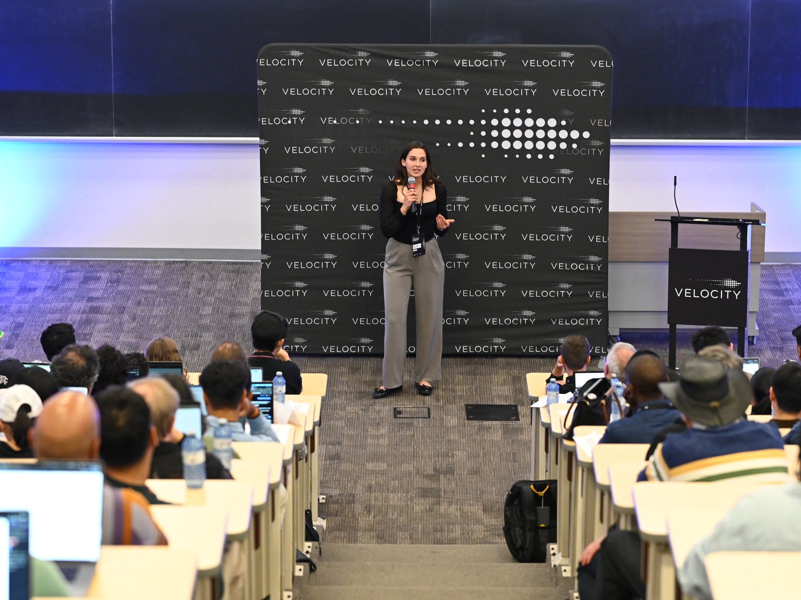 Presenting to a full lecture hall in front of a Velocity backdrop